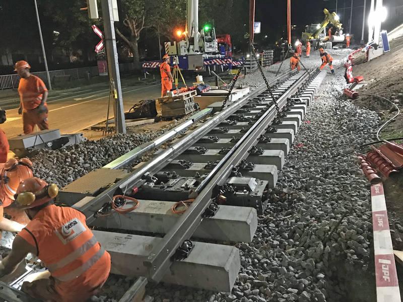 Bauarbeiter arbeiten an neuen Gleisen in der Nacht. ein Kran hebt Gleise an.